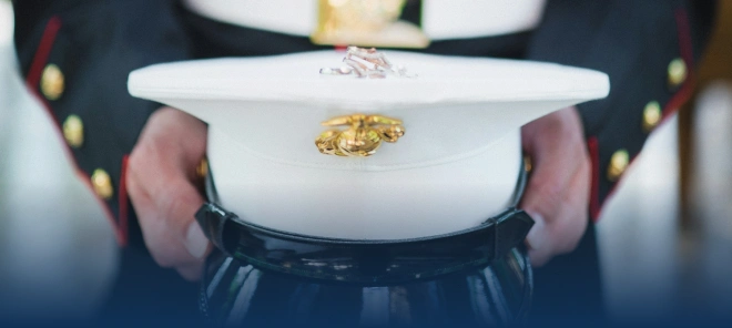 Close-up of a U.S. Marine in a dress blue uniform holding a white cover featuring the gold Eagle, Globe, and Anchor emblem.